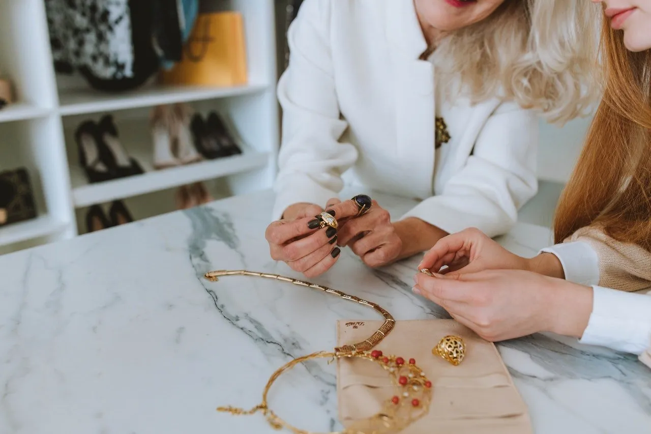 Dos mujeres observan joyas y pulseras de oro sobre una mesa de mármol en una tienda