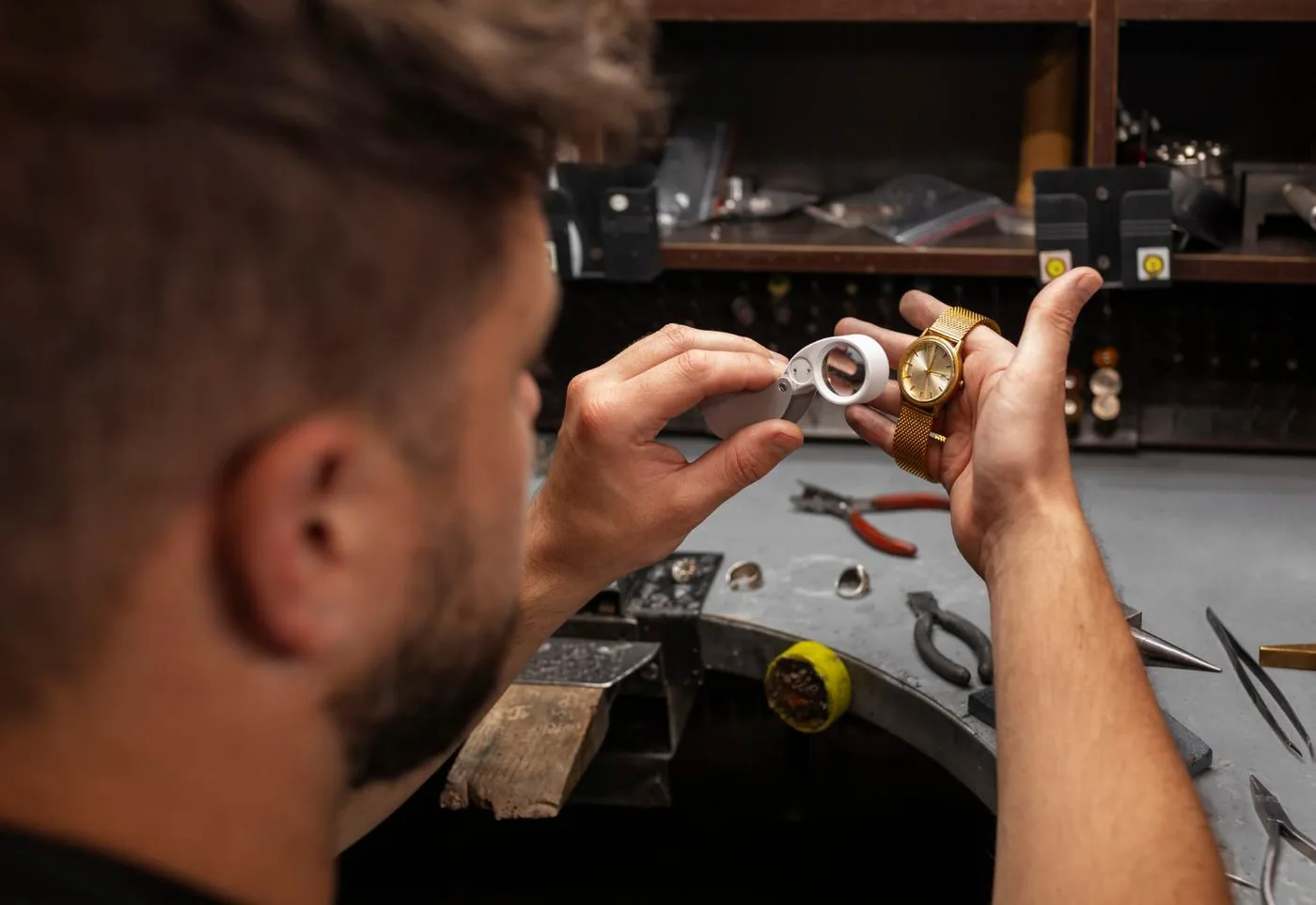 Horlogemaker beoordeelt met een loep het glas van een gouden horloge aan de werkbank van het atelier