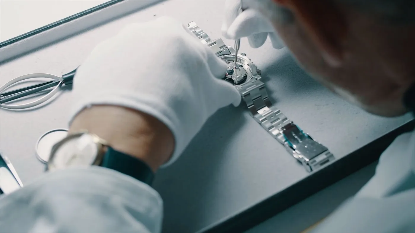 Horlogemaker met witte handschoenen demonteert het uurwerk van een stalen horloge tijdens een reparatie