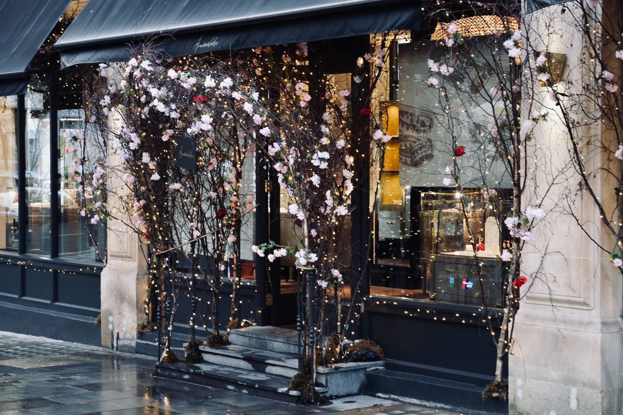 Sfeervol versierde etalage van een juwelierszaak met bloemen en lichtjes die voorbijgangers naar binnen trekt