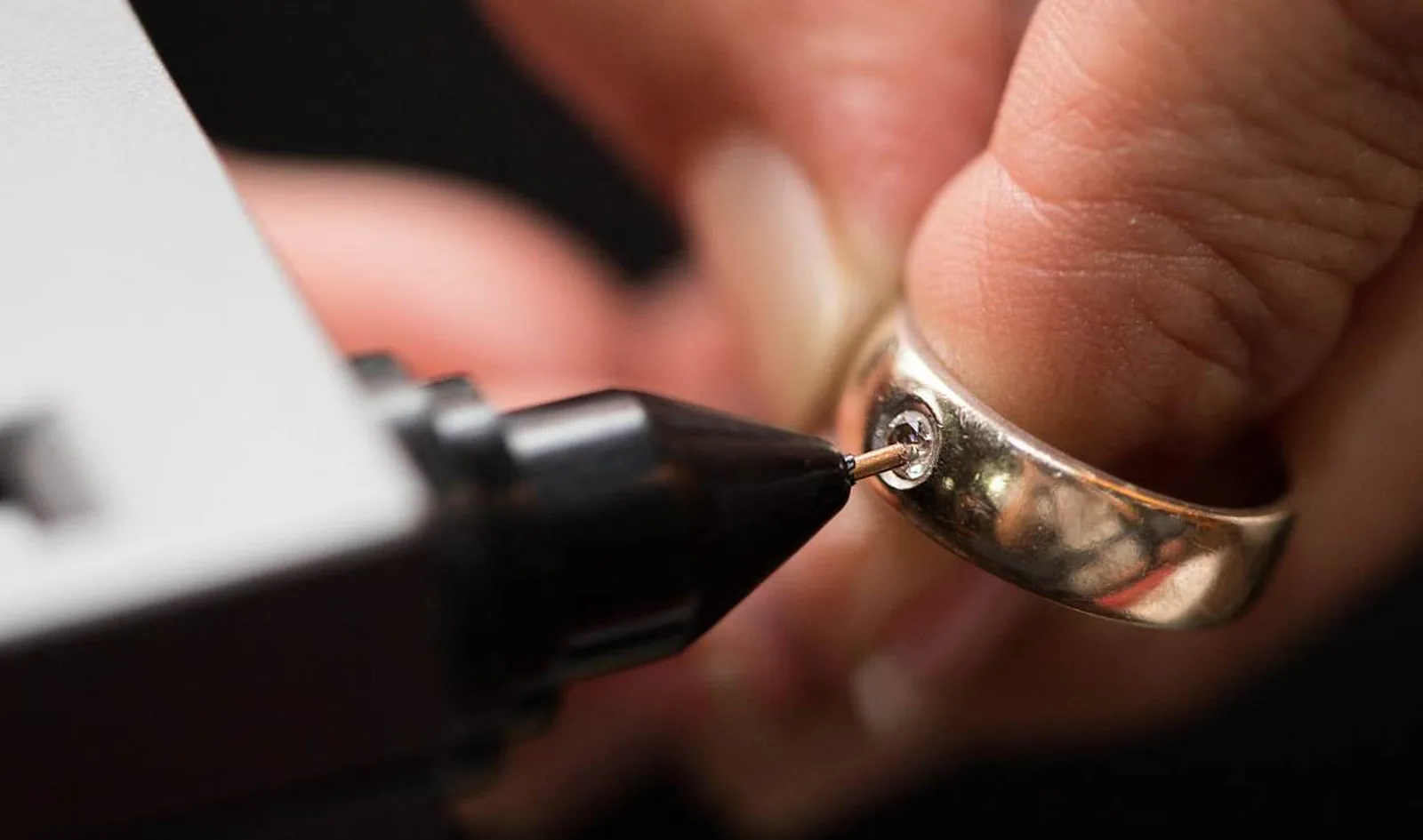 Goudsmid zet met een vatzetter een steen in een gouden ring tijdens een reparatie in het atelier van een juwelier